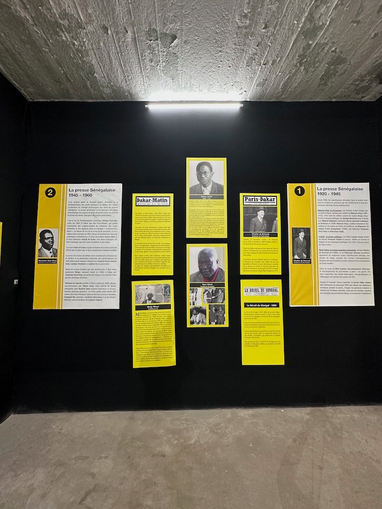 Yellow panels with portraits hang on a black wall in a museum room.