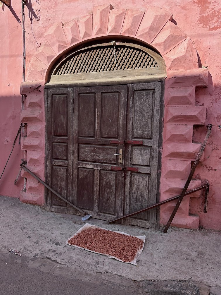 An old wooden door stands in a pink wall in Saint-Louis.