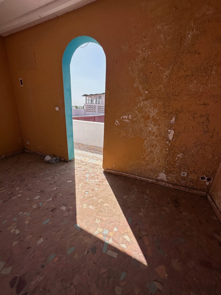 A turquoise arch door opens from an orange room to a terrace in Saint-Louis.