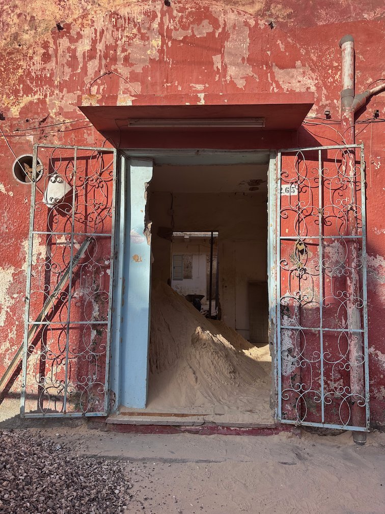 Sand fills the open door of an old red building in Saint-Louis.