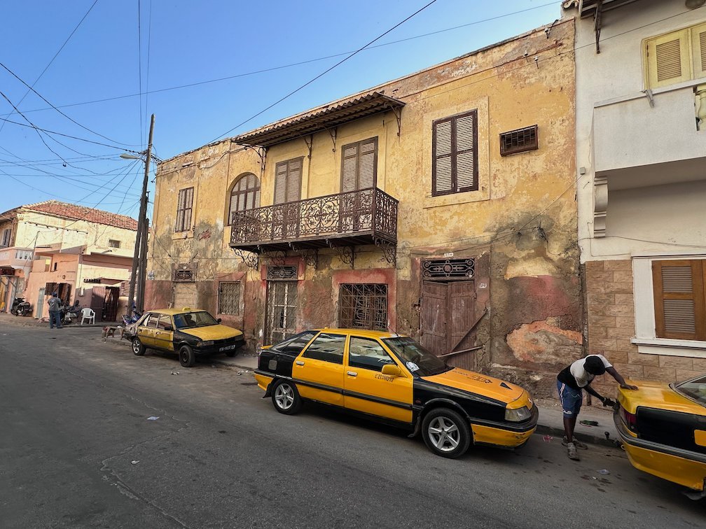 Yellow taxis park in front of an old yellow house in Saint-Louis.