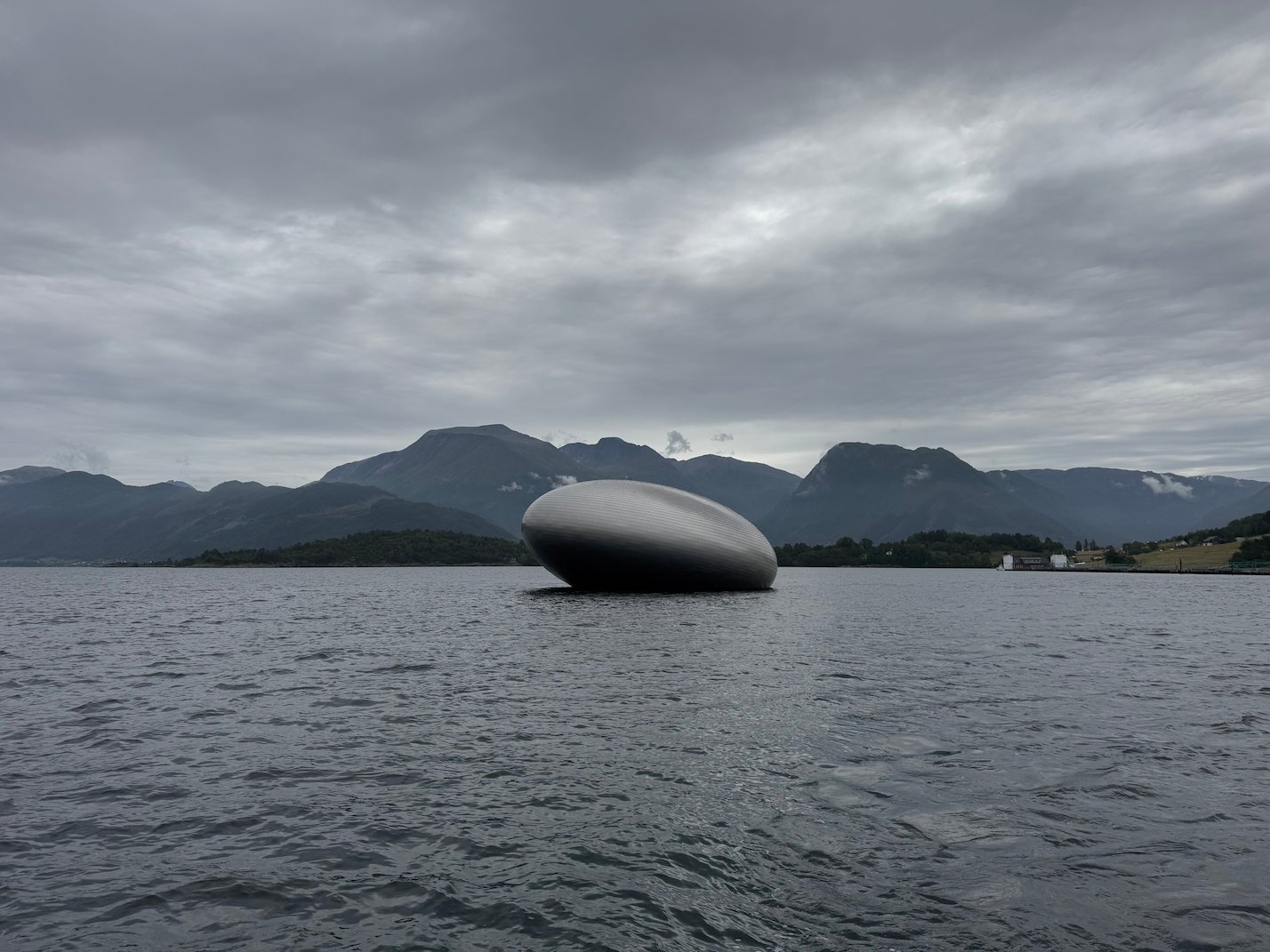 Salmon Eye, the egg-shaped steel visitor center, on the Hardangerfjord under grey clouds
