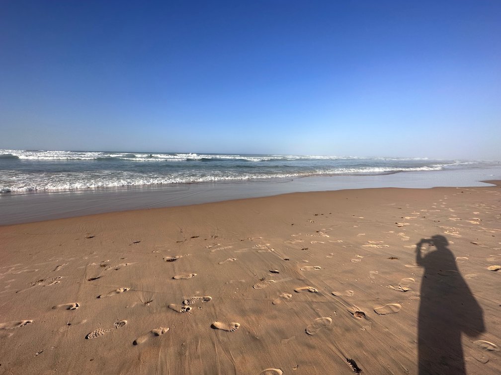 A shadow of a person falls on the sand near the waves.