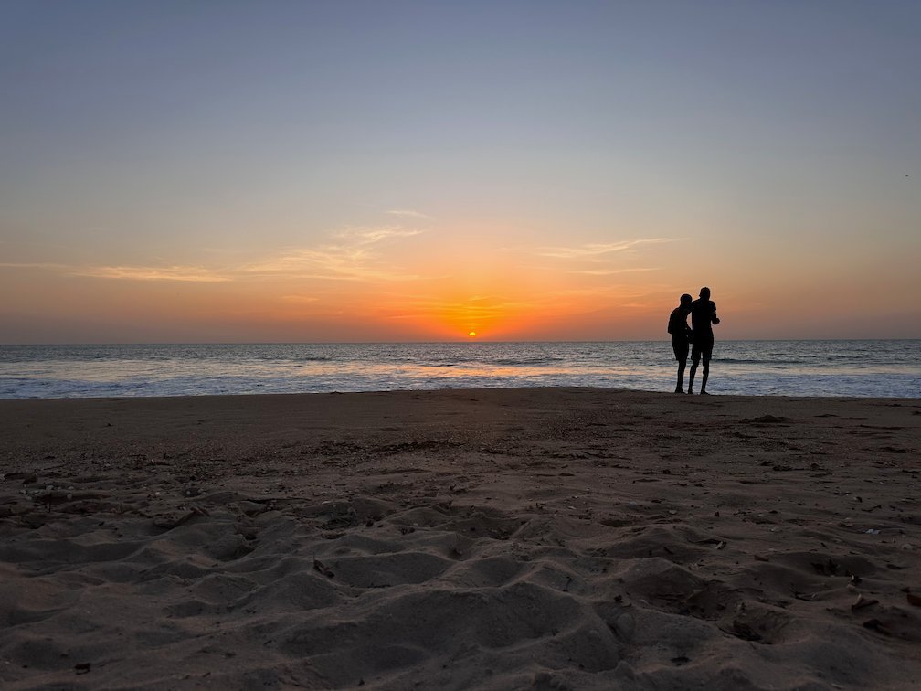 A couple stands on the beach and looks at the sunset in Saly.