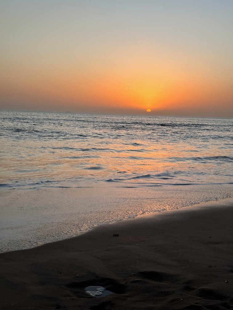 The sun sets over the ocean and a quiet beach in Saly.