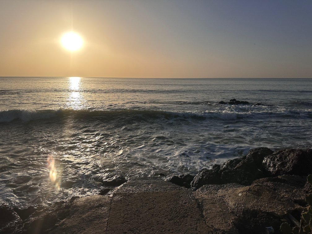 The sun shines over waves and dark rocks in Saly.