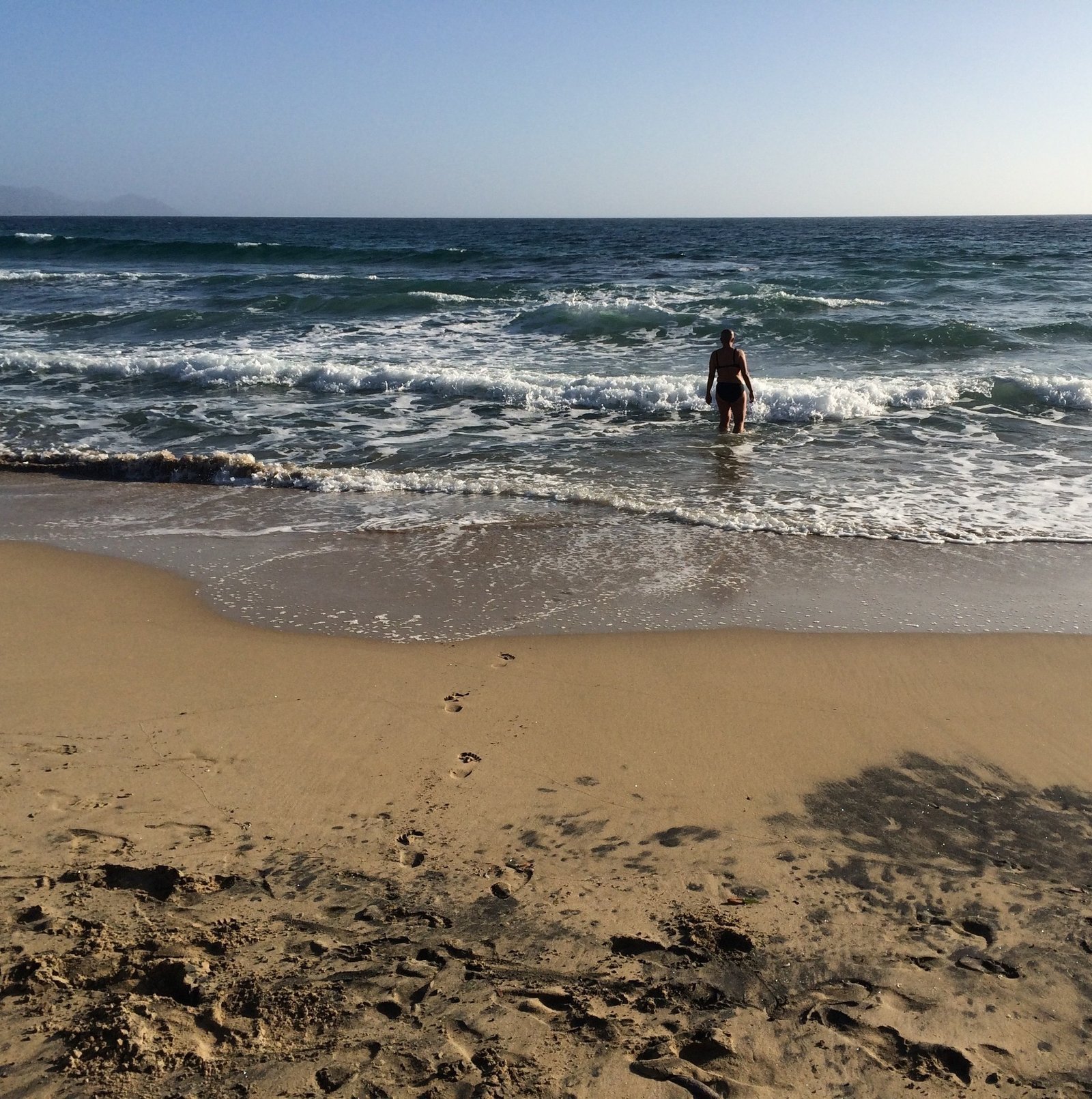 A swimmer stands in the waves at a sandy beach in Sardinia.
