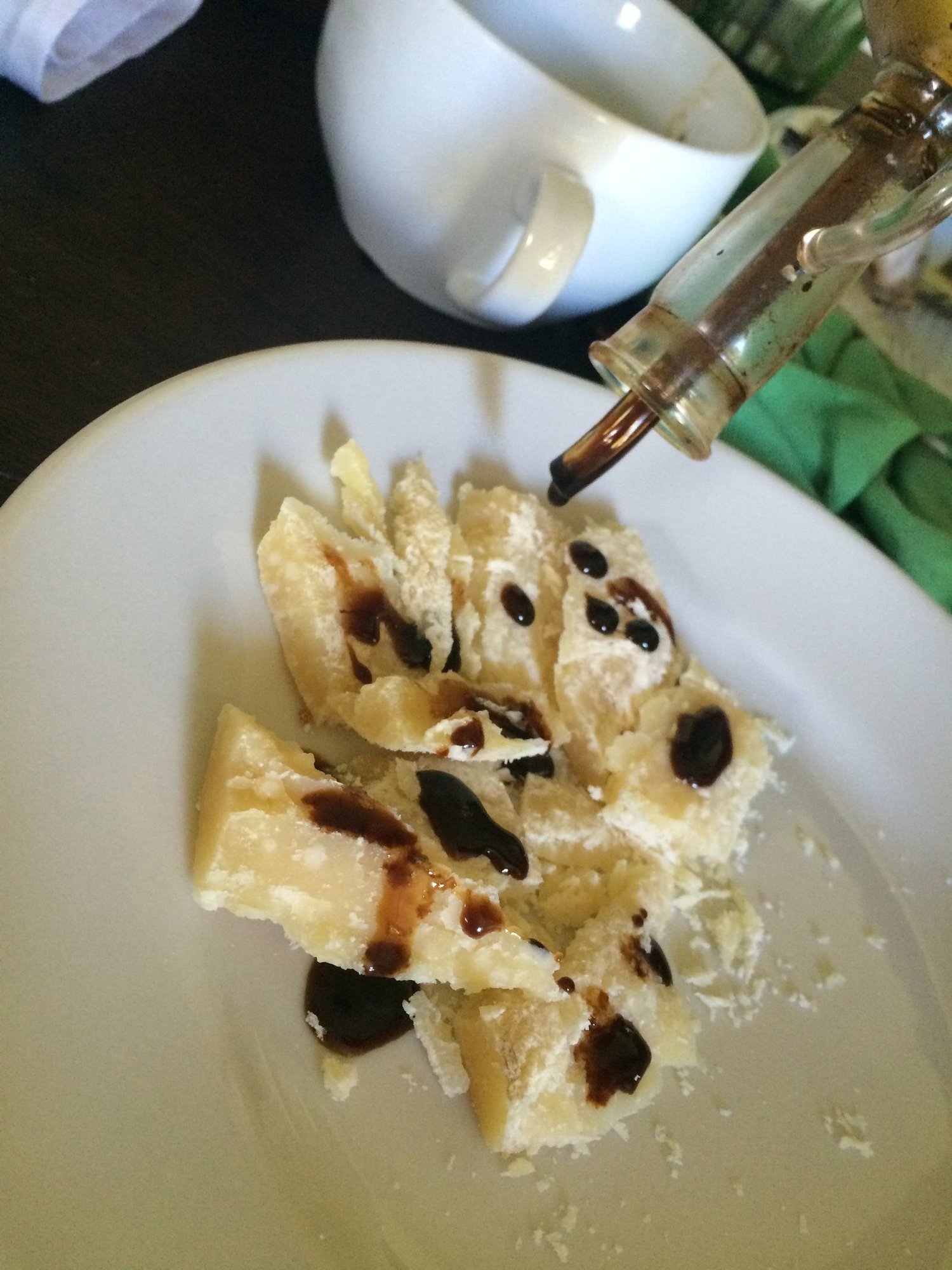 Thin slices of cheese with balsamic vinegar and oil lie on a white plate.