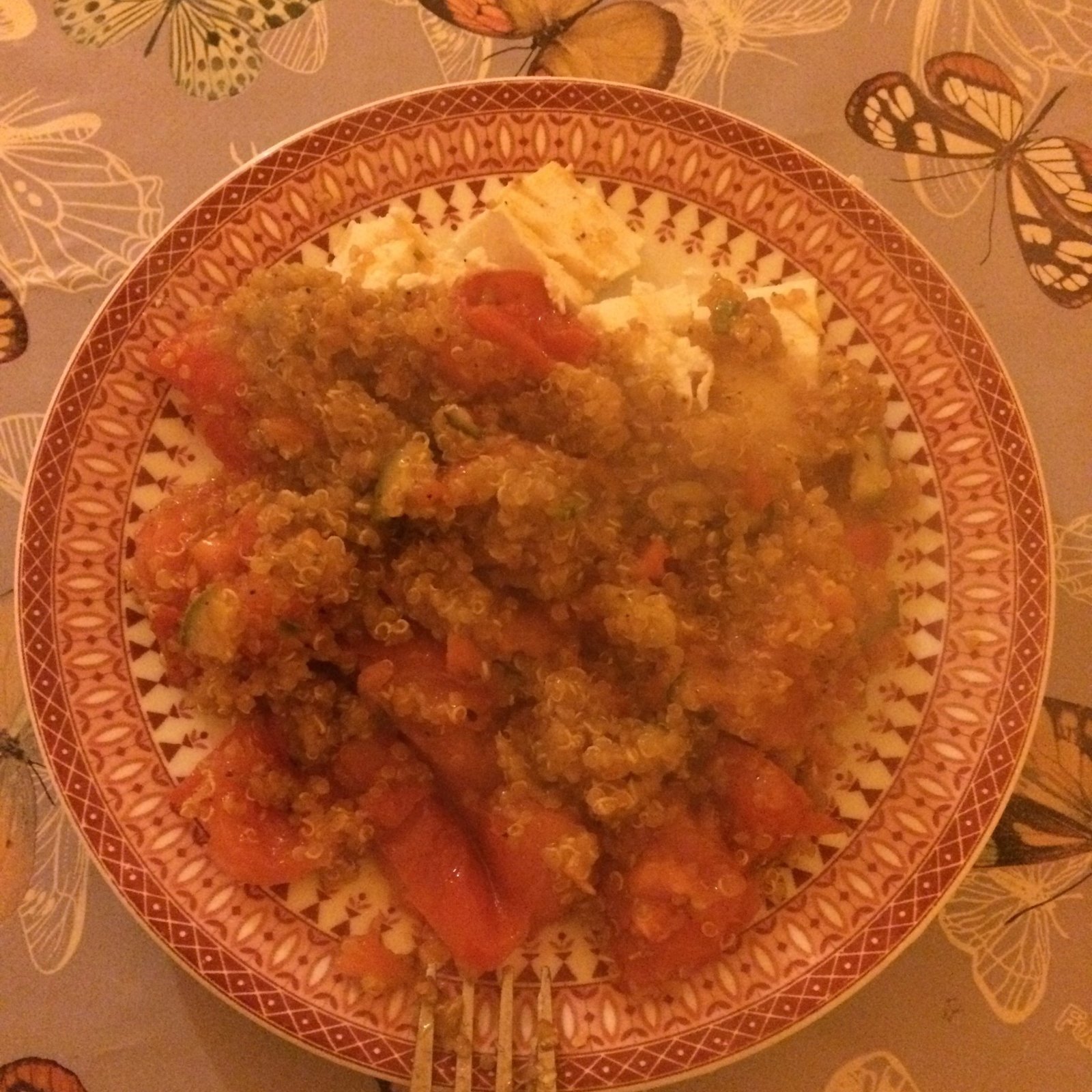 A plate of cooked vegetables and grains stands on a table with a butterfly cloth.