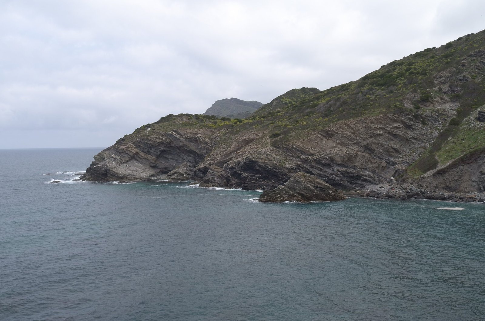A green headland with steep cliffs reaches into the sea in Sardinia.