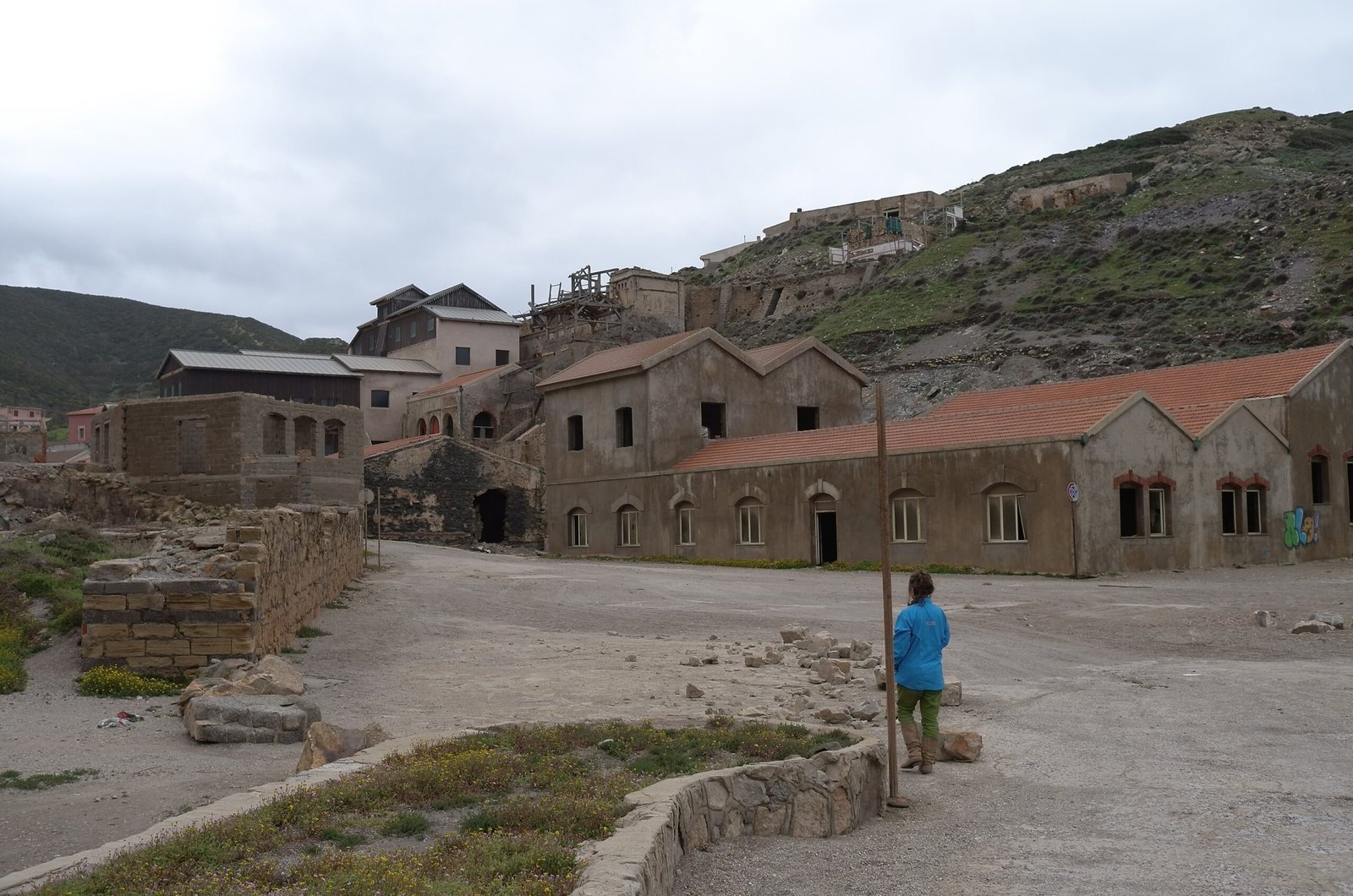 Old stone mine buildings stand on a hillside near the coast of Sardinia.