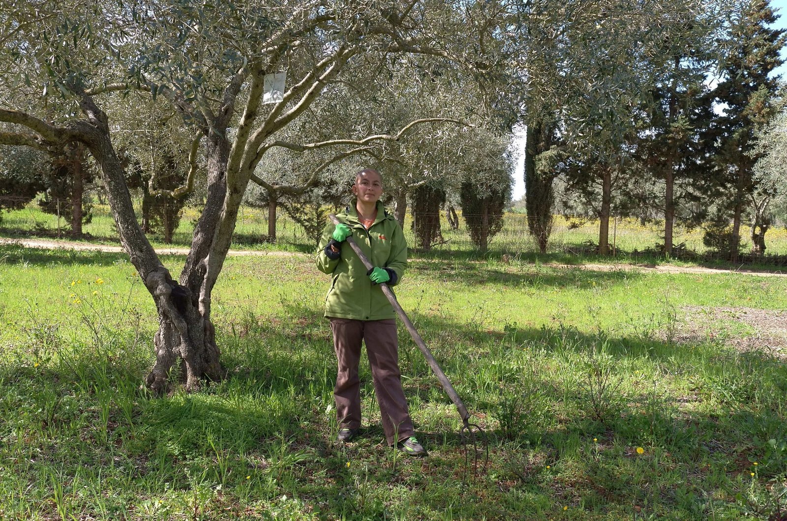 Zayera Khan stands with a rake in an olive grove on a farm in Sardinia.