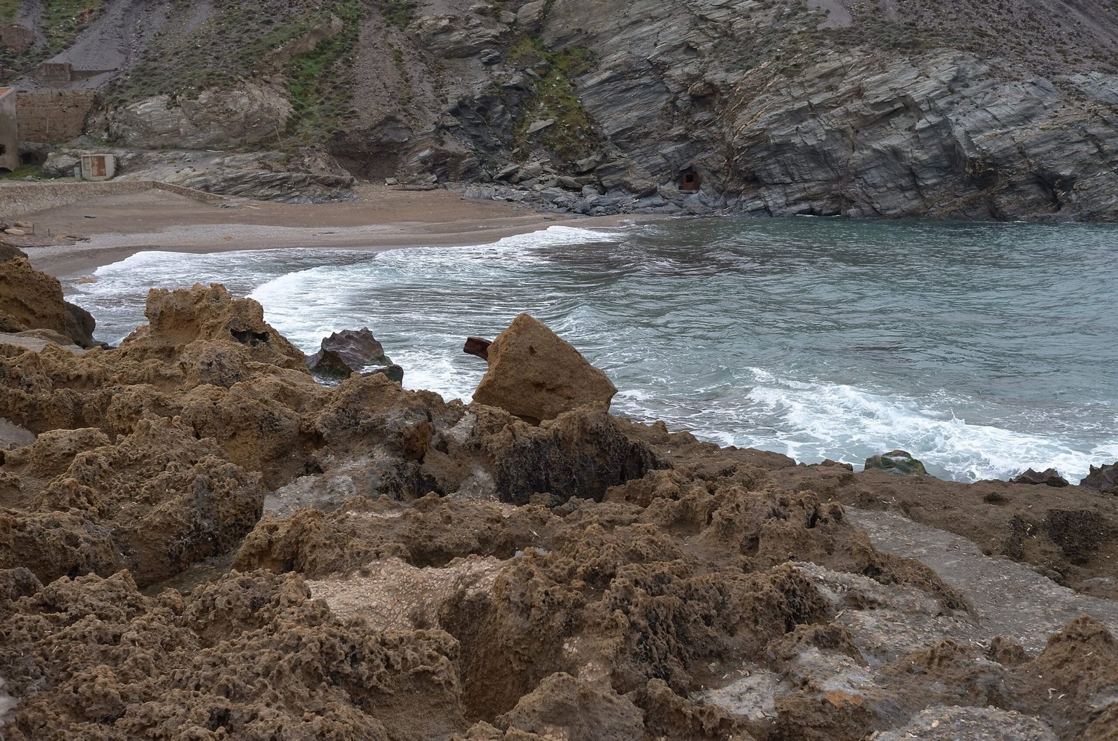 Waves break on brown rocks in a small cove on the coast of Sardinia.