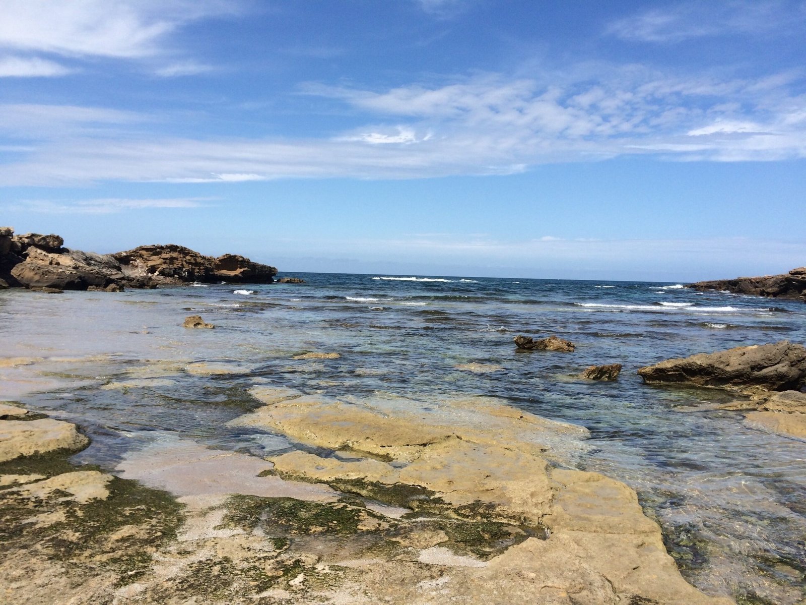 Clear water and flat yellow rocks meet on a rocky shore in Sardinia.