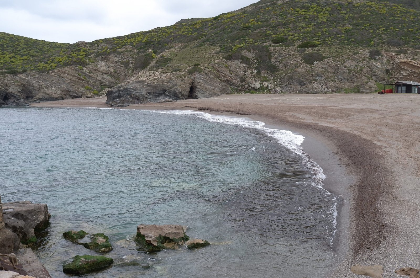 A small sandy cove with calm water lies between green hills in Sardinia.