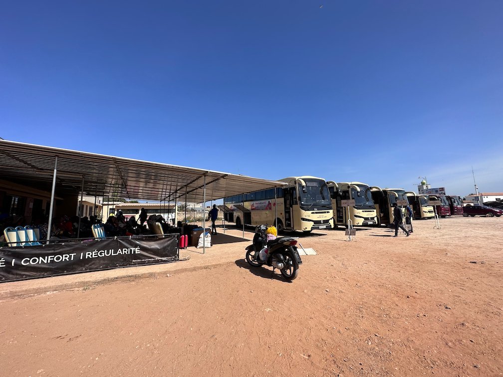Coach buses wait under a long roof at a bus station in Senegal.