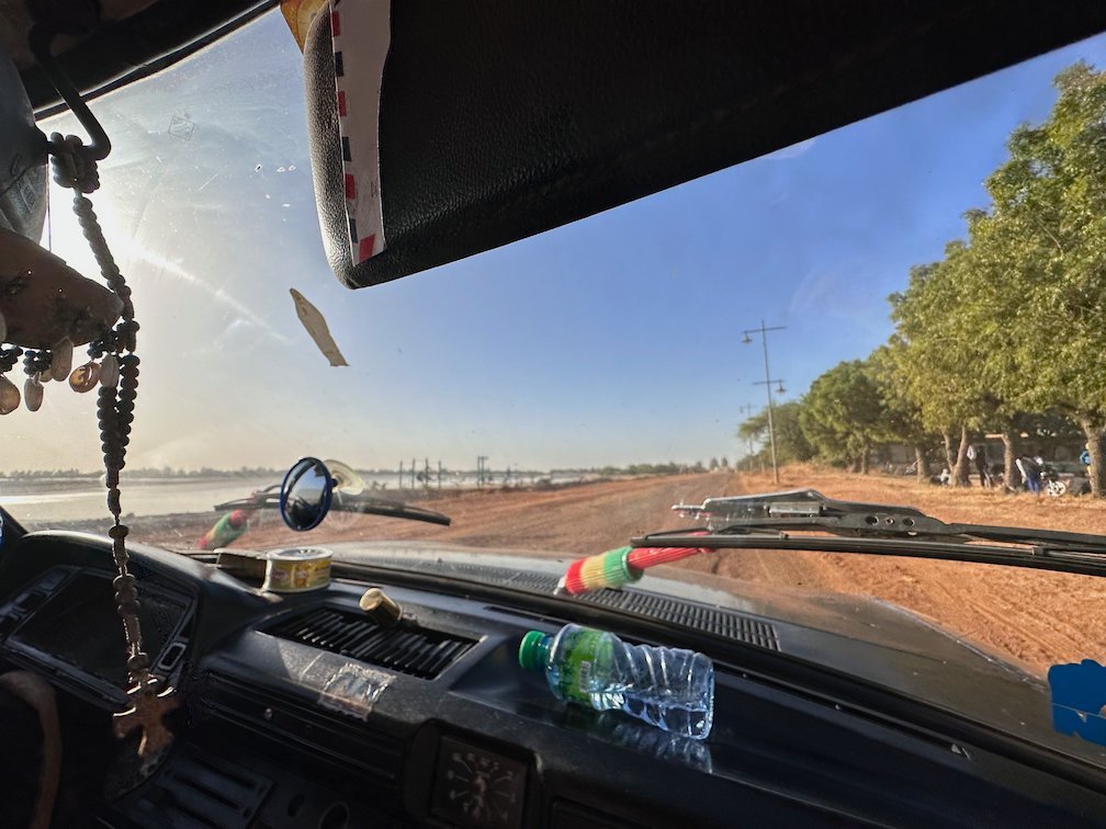 A road with trees is seen through the windshield of a bush taxi.