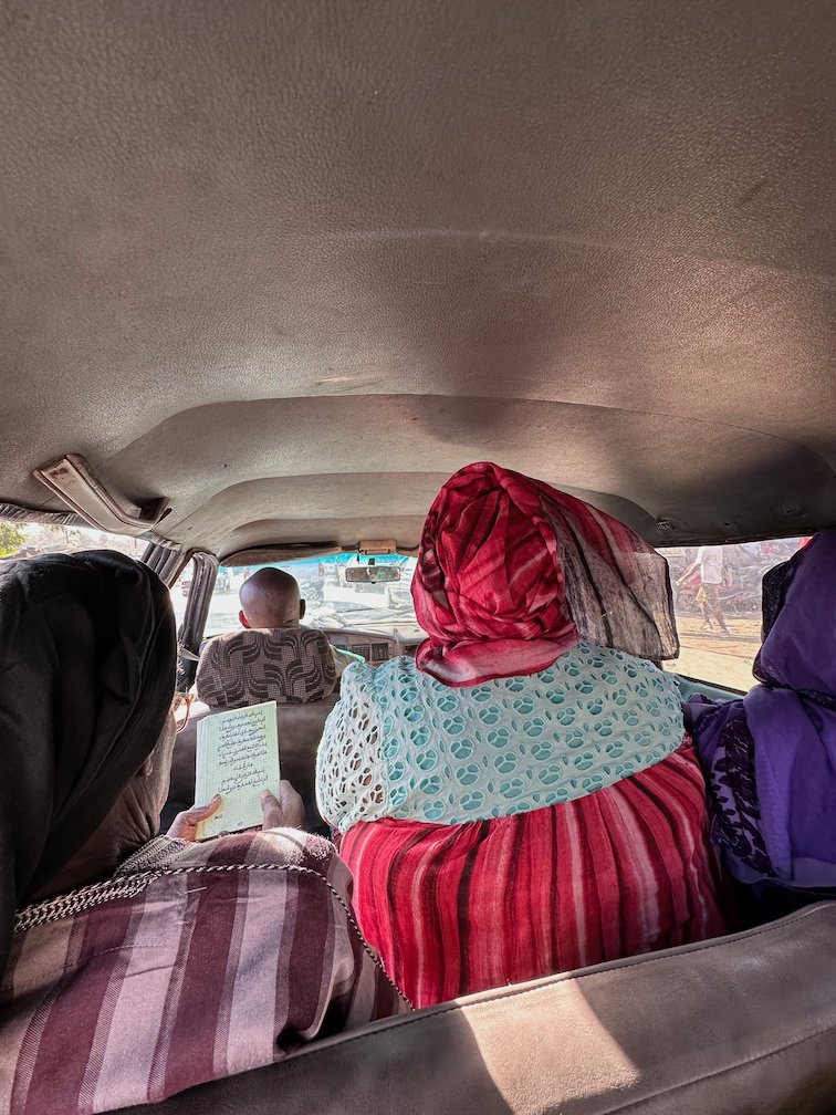 Women in colorful clothes sit in the back of a bush taxi.