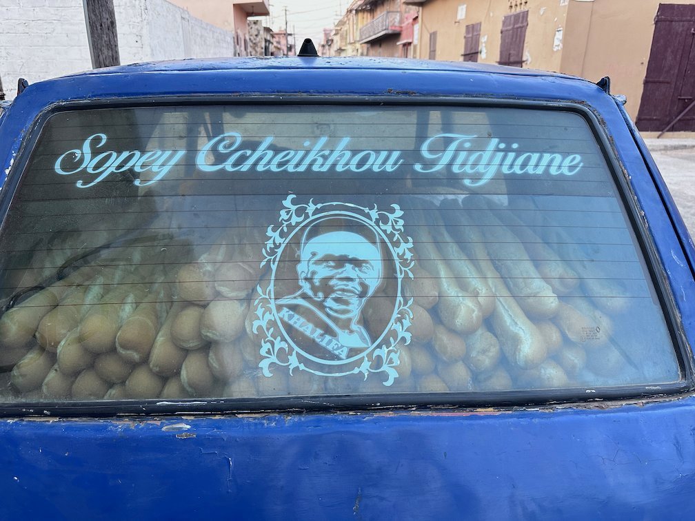 A blue car has a decal of a religious leader on its back window.