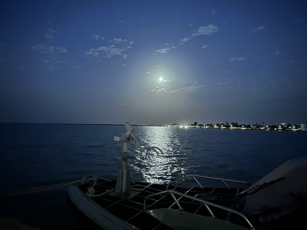 The moon shines on the water next to a boat at night in Senegal.