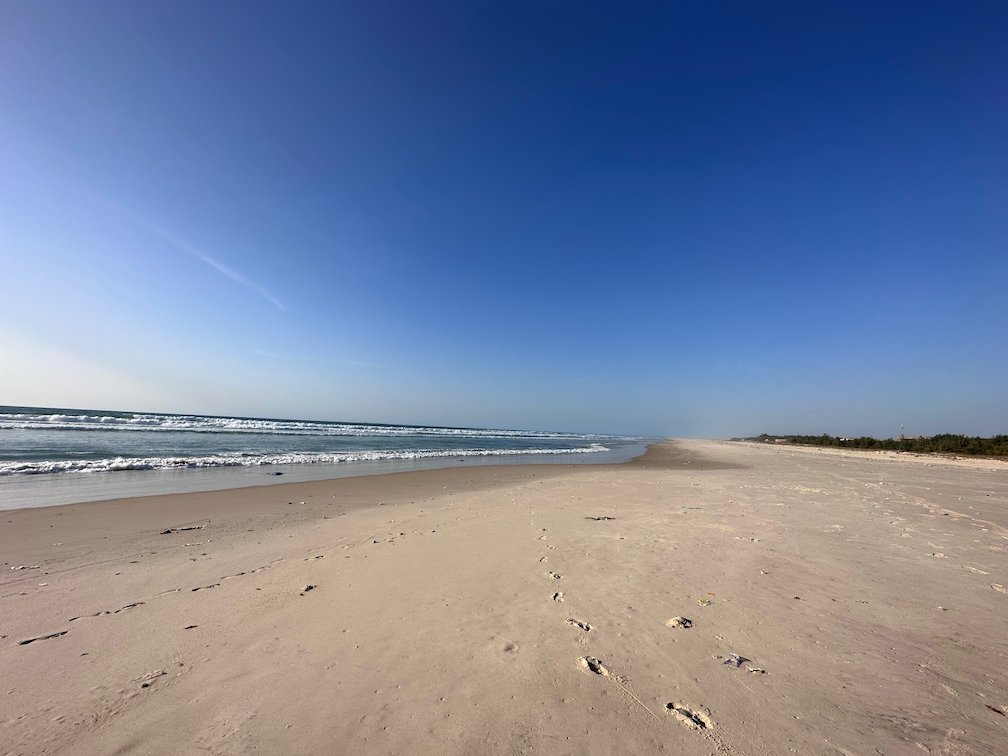 An empty beach with footprints runs along the ocean in northern Senegal.