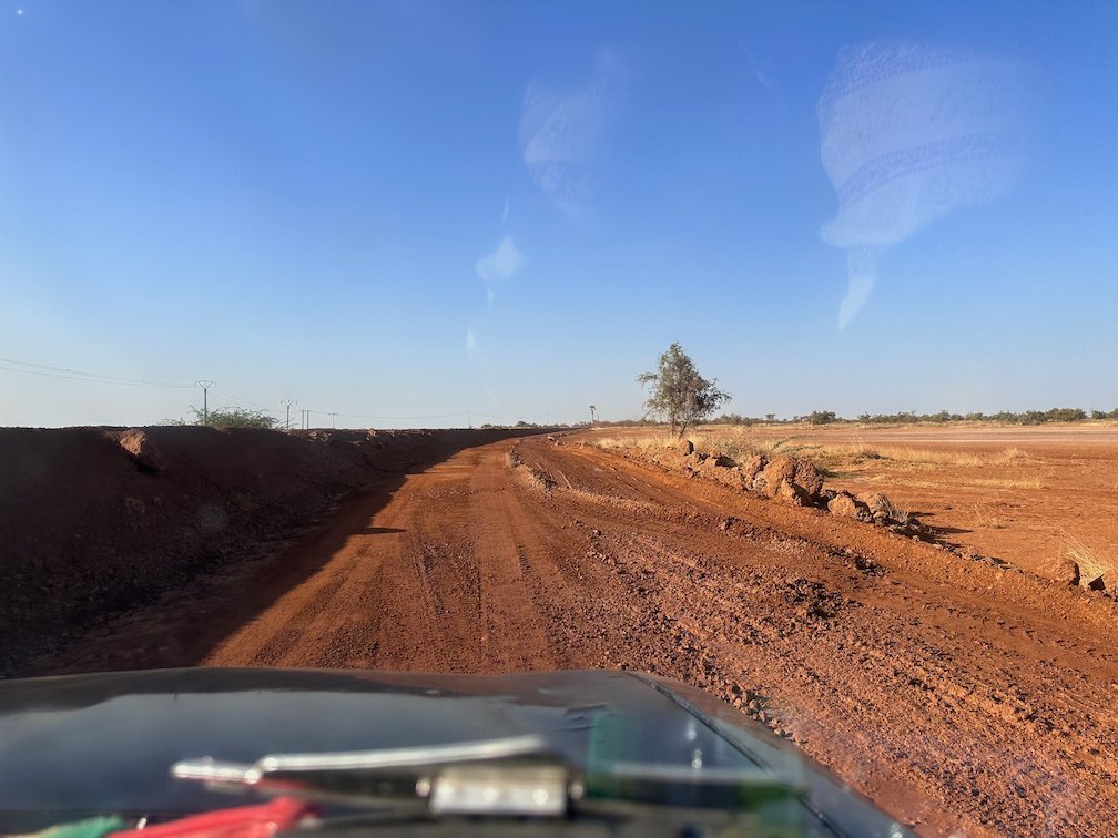 A red dirt road runs through dry land in Senegal.