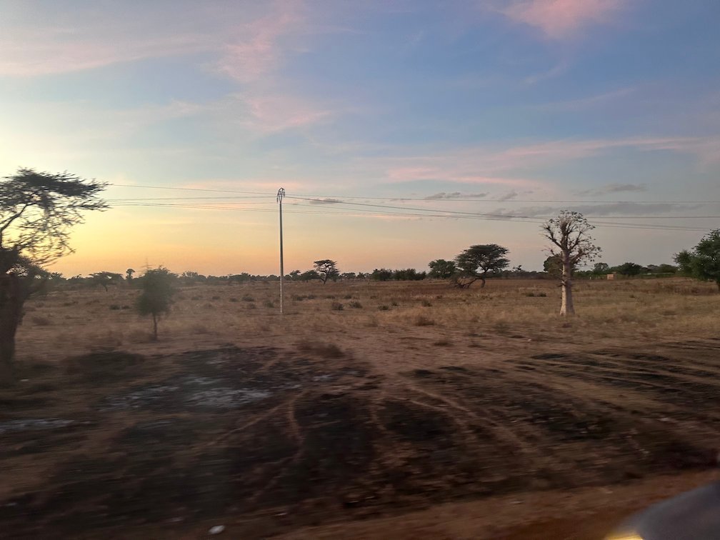 The sun sets over dry savanna with baobab trees in Senegal.