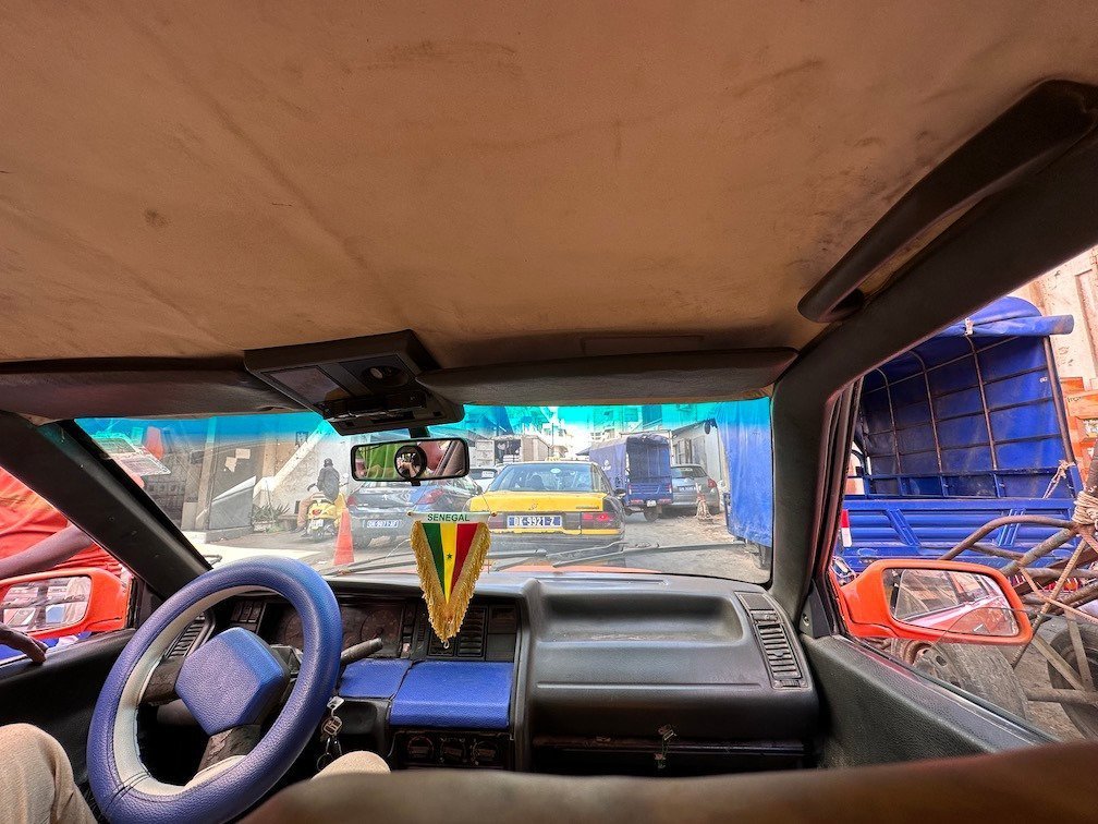 The dashboard of an old shared taxi faces a busy street in Senegal.