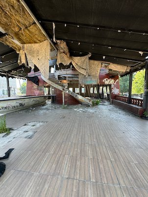 Torn fabric hangs from the roof over an empty wooden deck by the river in Skopje.