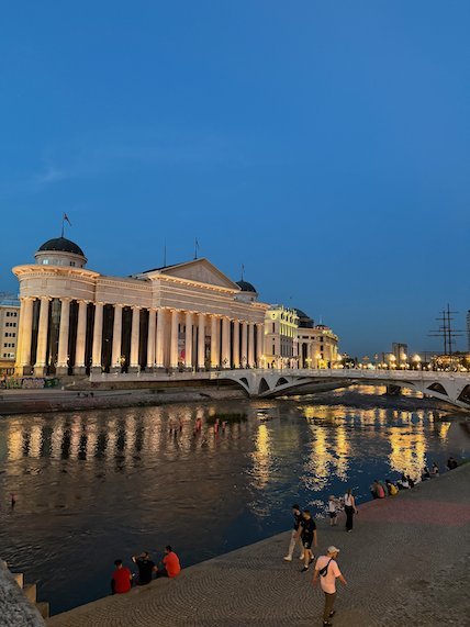 The Archaeological Museum and a bridge reflect in the Vardar River at dusk in Skopje.