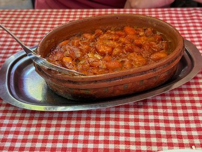 Baked beans in a clay dish sit on a red checked tablecloth in Skopje.
