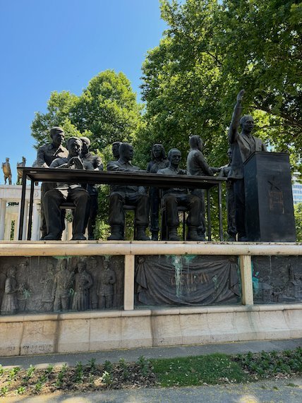 Bronze figures sit at a long table above a relief wall in Skopje.