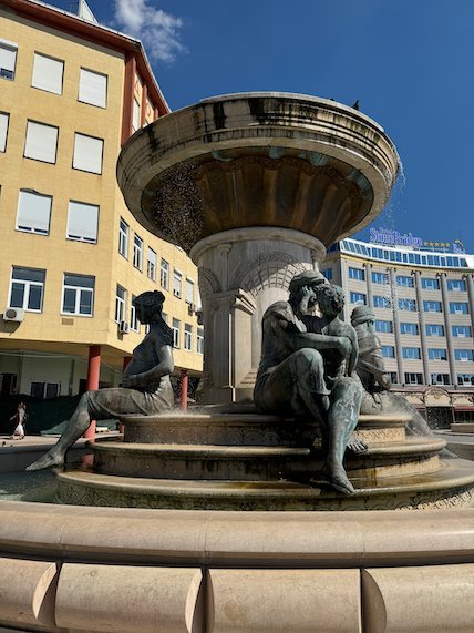 A bronze fountain with figures of women and children stands on a square in Skopje.