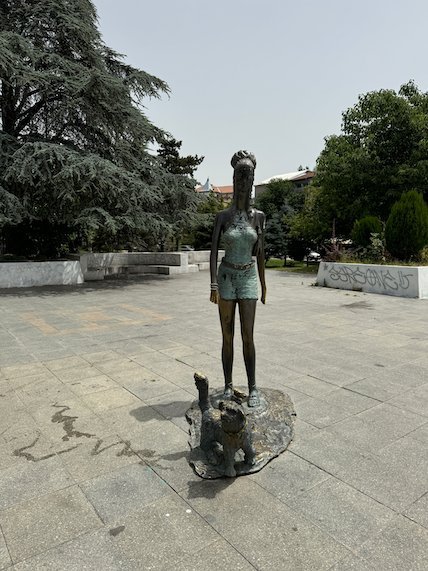 A bronze statue of a girl stands on a paved square in Skopje.