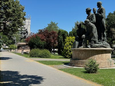 A bronze statue group stands beside a path in a green park in Skopje.
