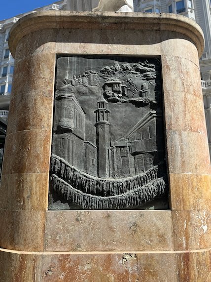 A bronze relief shows towers and buildings on a stone monument base in Skopje.