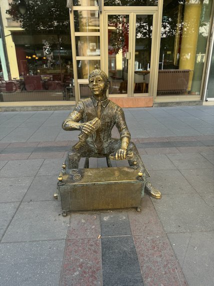 A bronze statue of a seated craftsman stands on a pedestrian street in Skopje.