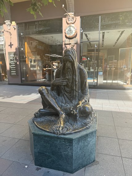 A bronze statue of a seated figure stands on a street in central Skopje.
