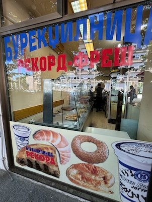 A bakery window with Cyrillic letters shows pictures of burek and pastries in Skopje.