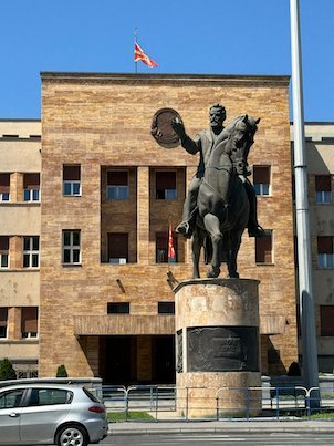 A bronze rider on a horse stands in front of a large government building in Skopje.