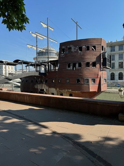 A wooden galleon with masts stands on the riverbank in central Skopje.