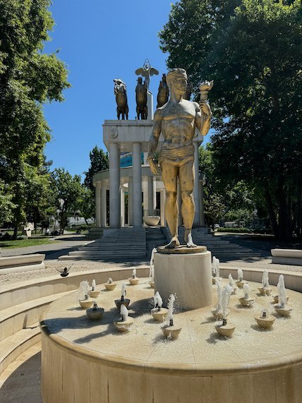 A gold statue holds a torch on a fountain in a park in Skopje.