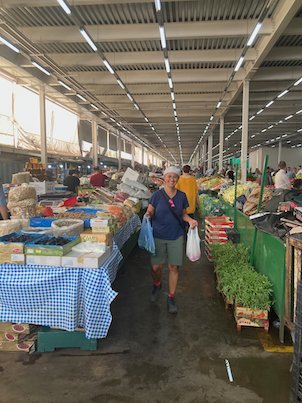 A traveler walks with shopping bags along an aisle of a covered market in Skopje.