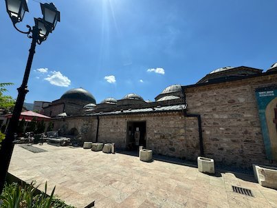 Lead domes cover a long stone Ottoman bathhouse beside a square in Skopje.