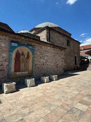 An old stone Ottoman bathhouse with lead domes stands on a paved square in Skopje.