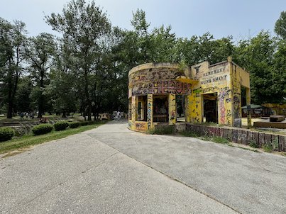 A small round kiosk covered in graffiti stands beside a path in a park in Skopje.