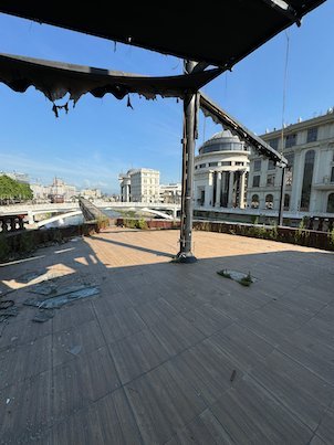An empty wooden deck looks toward a domed building across the river in Skopje.