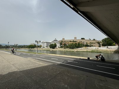 A riverside path runs under a bridge along the Vardar River with Kale Fortress behind in Skopje.