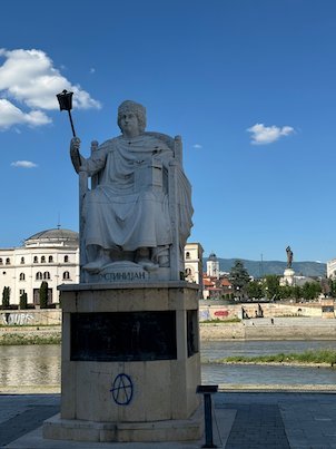 A white statue of a seated emperor stands by the Vardar River in Skopje.