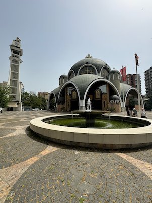 St. Clement of Ohrid Church with round domes and a bell tower stands behind a fountain in Skopje.
